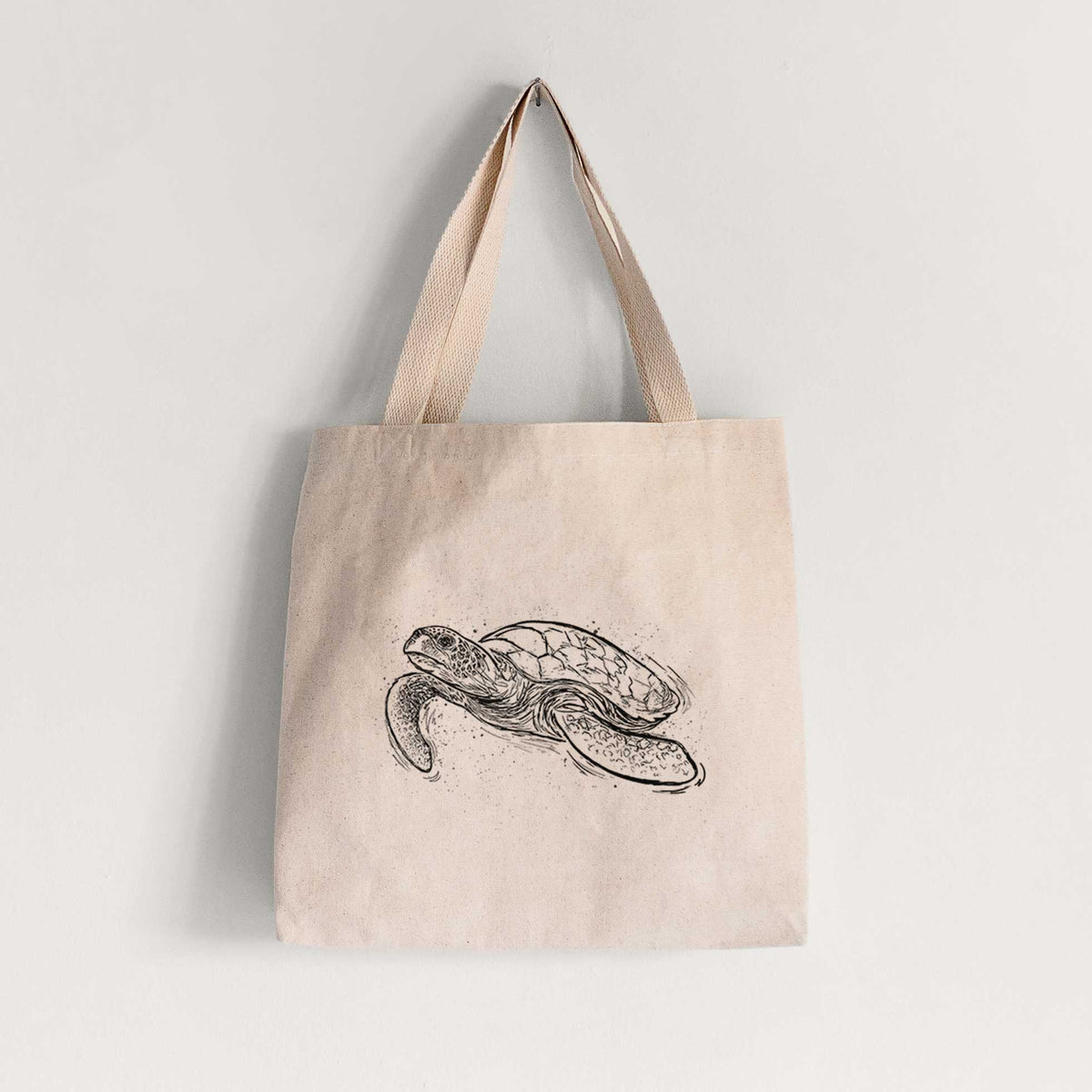 Natural canvas tote bag printed with a black ink illustration of a hawksbill sea turtle swimming, with a patterned shell.