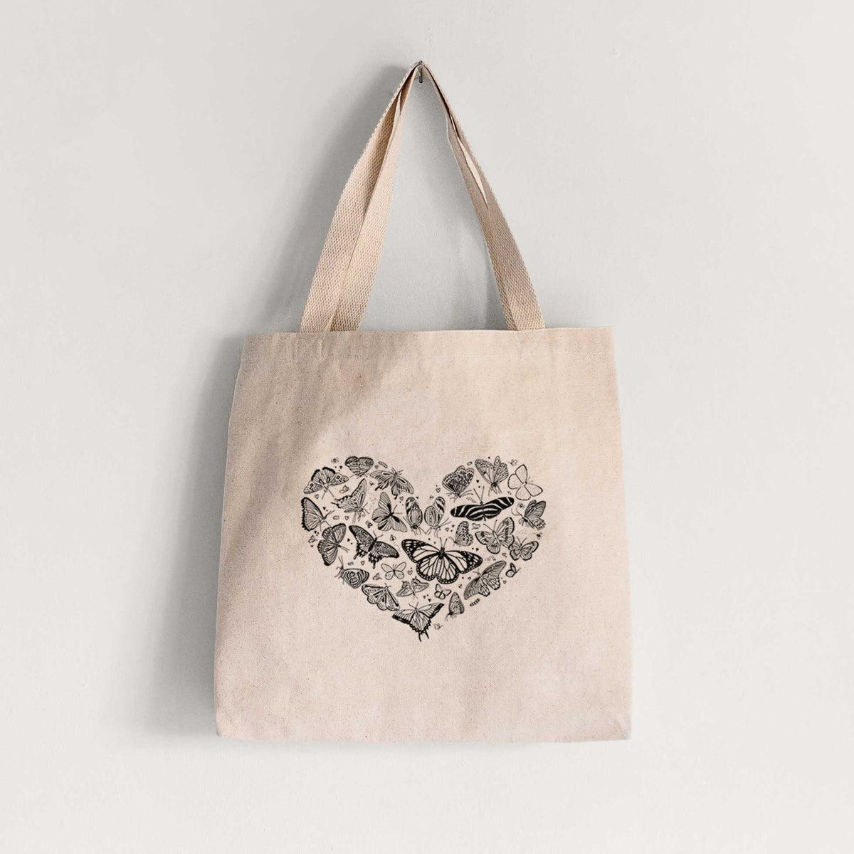Natural canvas tote bag printed with a heart shape filled with small black ink butterflies and moths.