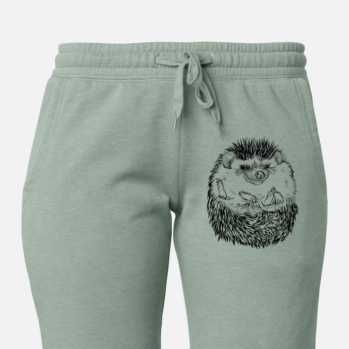 Front of sage green Cali Wave sweatpants, printed with a detailed black ink illustration of a hedgehog curled up and facing forward on the leg.