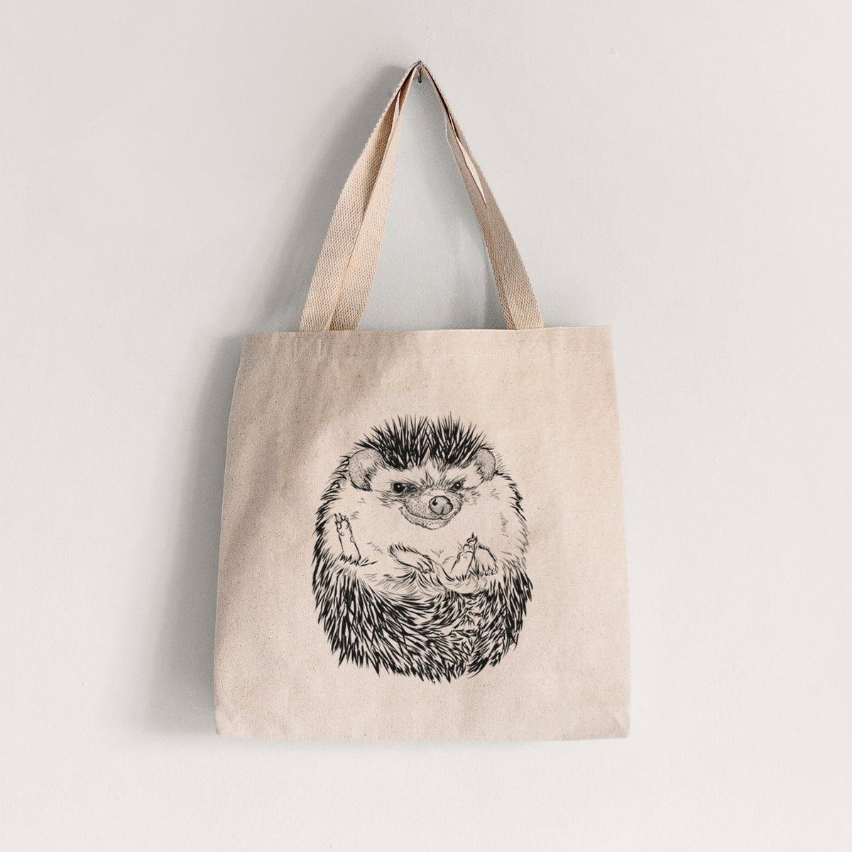 Natural canvas tote bag printed with a detailed black ink illustration of a hedgehog curled up and facing forward.
