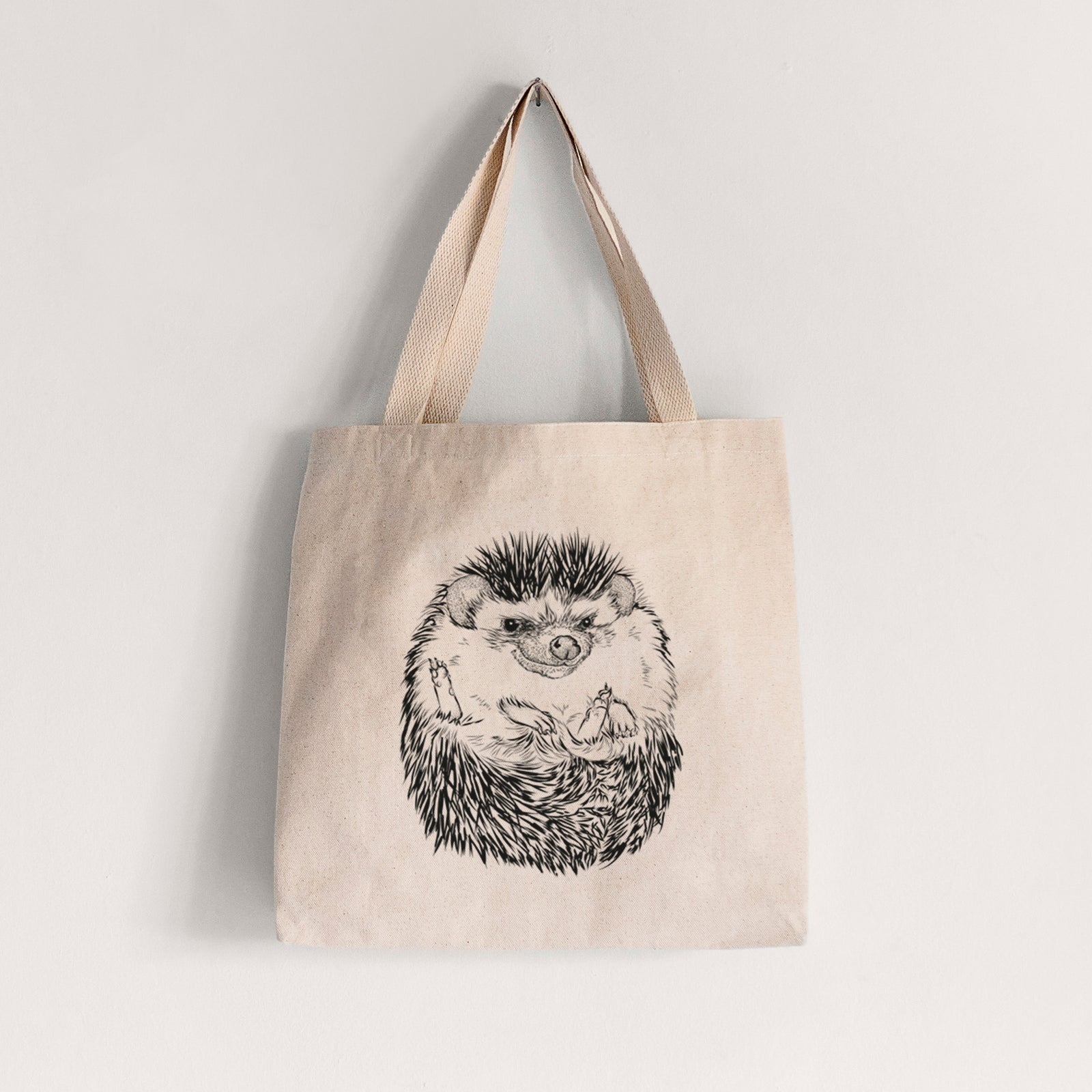 Natural canvas tote bag printed with a detailed black ink illustration of a hedgehog curled up and facing forward.