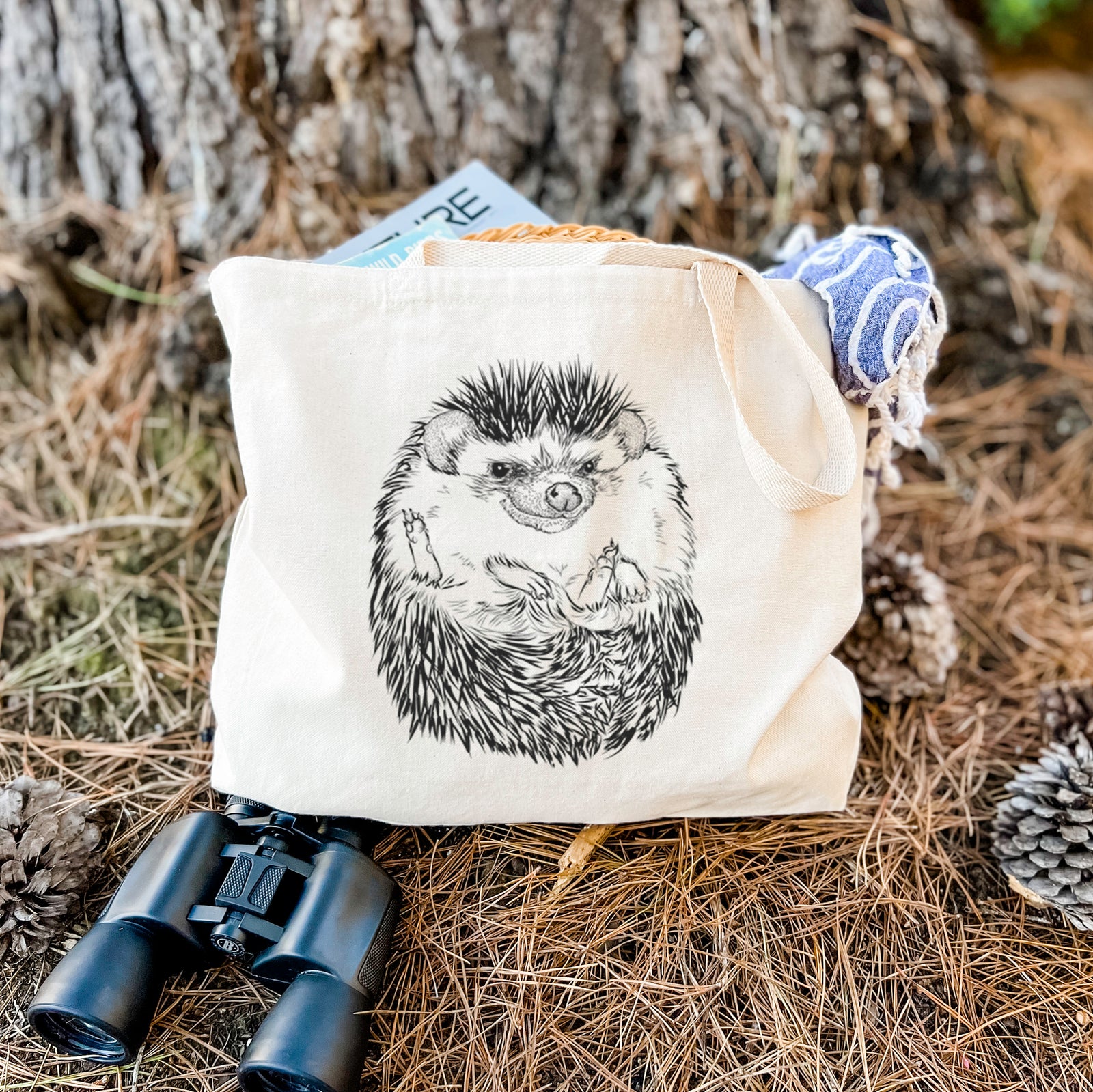 Natural canvas tote bag printed with a detailed black ink illustration of a hedgehog curled up and facing forward.
