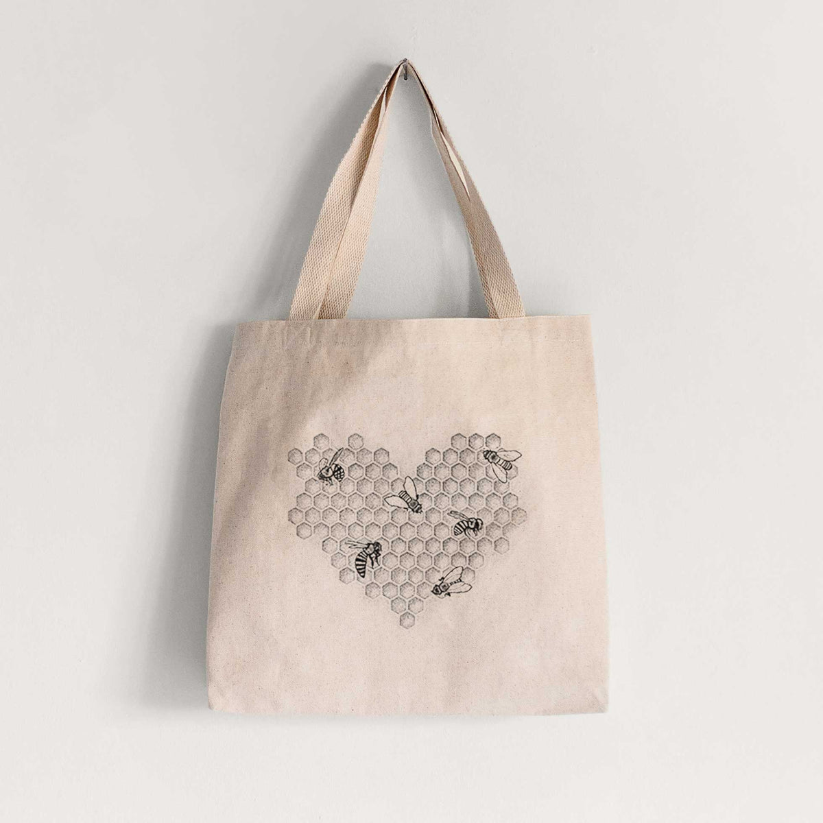 Natural canvas tote bag printed with a black ink heart made of honeycomb cells with small bees crawling across it.