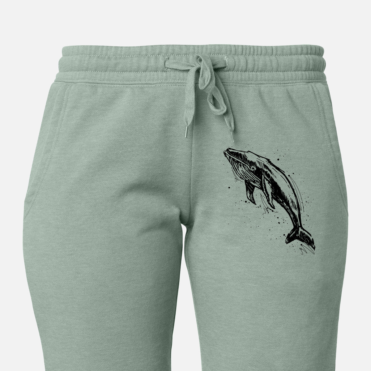 Front of sage green Cali Wave sweatpants, printed with a black ink illustration of a humpback whale diving, with ink splatters on the leg.