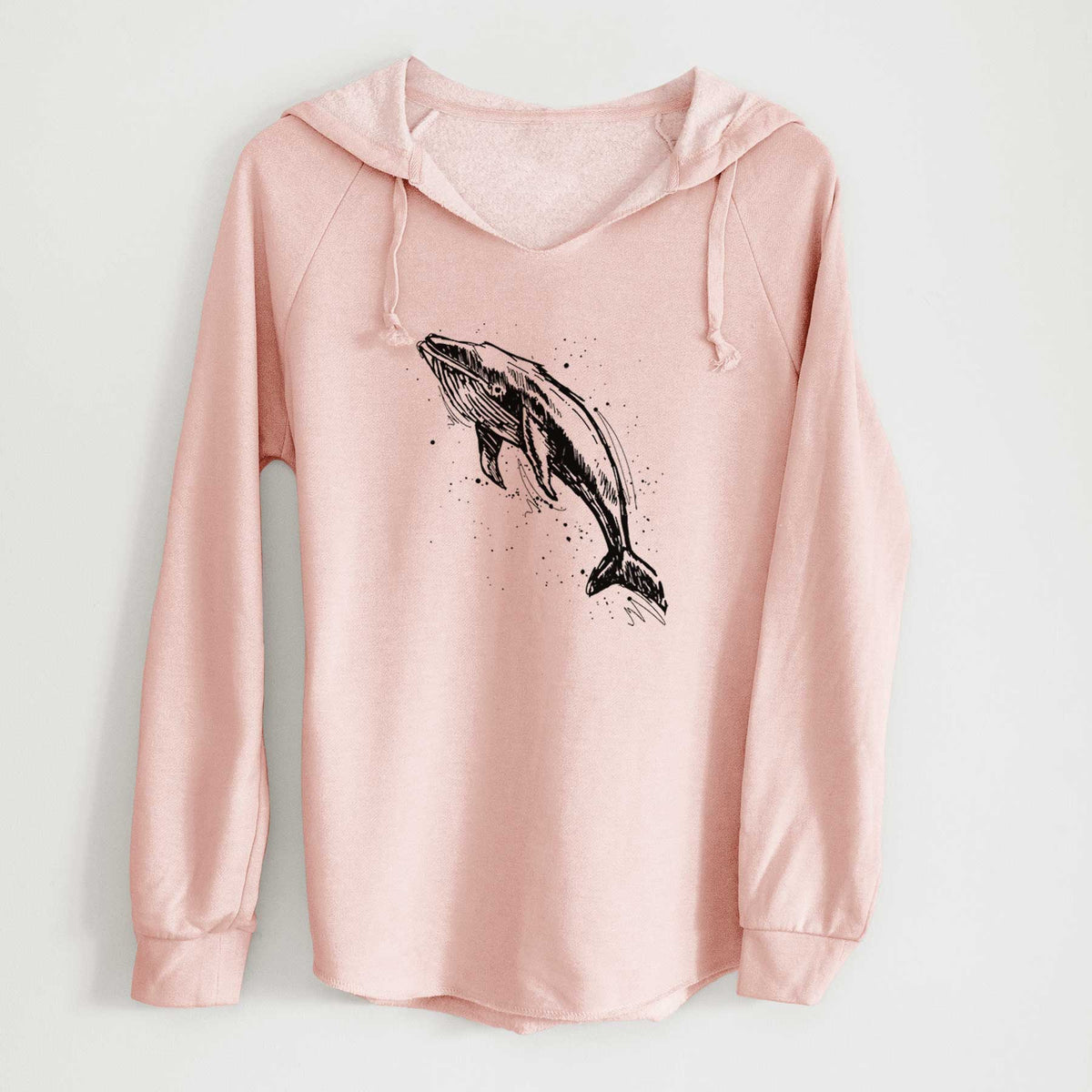 Blush pink women's Cali Wave hooded sweatshirt laid flat, printed with a black ink illustration of a humpback whale diving, with ink splatters.