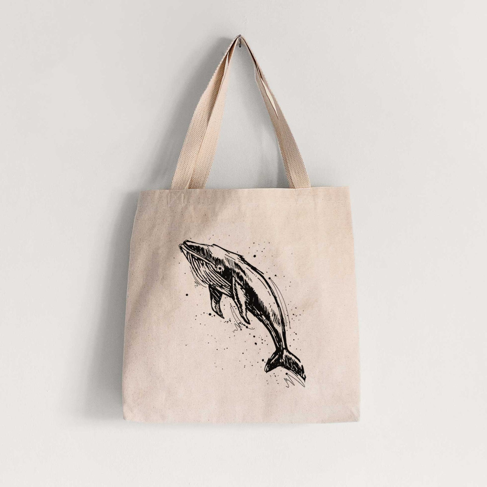 Natural canvas tote bag printed with a black ink illustration of a humpback whale diving, with ink splatters.