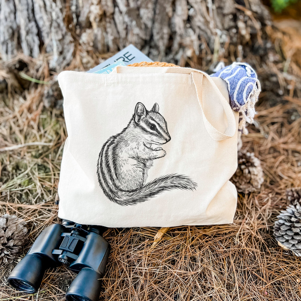 Canvas tote bag printed with a detailed black ink illustration of a least chipmunk sitting and holding food in its paws, resting on dry grass beside a pair of binoculars.