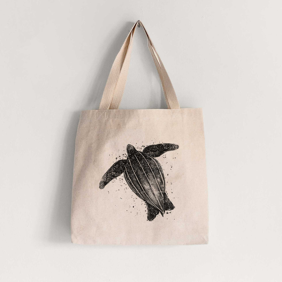 Natural canvas tote bag printed with a black ink illustration of a leatherback sea turtle swimming, with ink splatters.