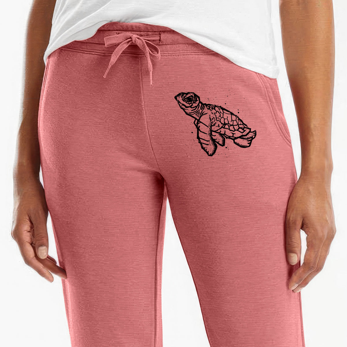Front of dusty rose Cali Wave sweatpants, printed with a black linocut-style illustration of a baby sea turtle with a patterned shell and ink splatters on the leg.