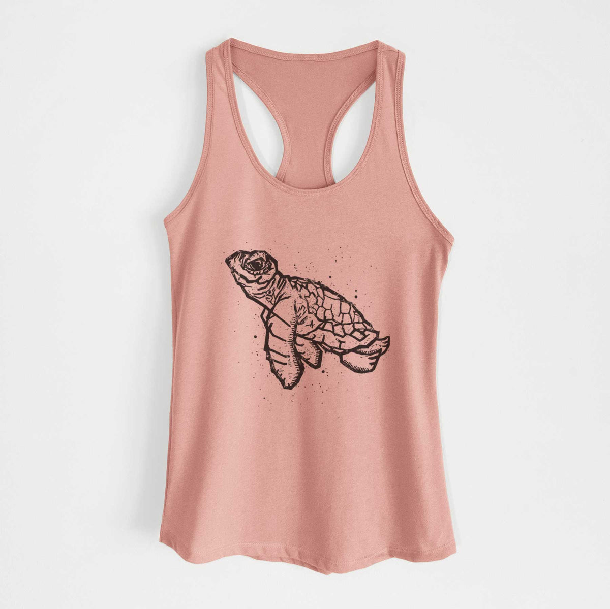 Desert pink women's racerback tank top laid flat, printed with a black linocut-style illustration of a baby sea turtle with a patterned shell and ink splatters.