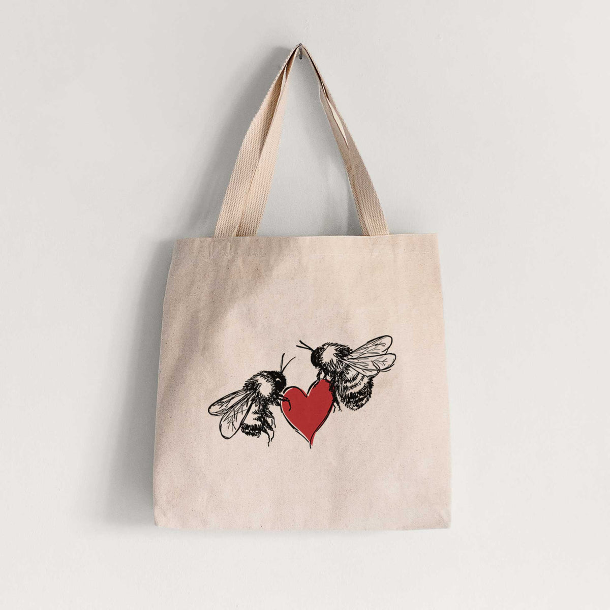 Natural canvas tote bag printed with a black ink illustration of two bees facing each other with a red heart between them.