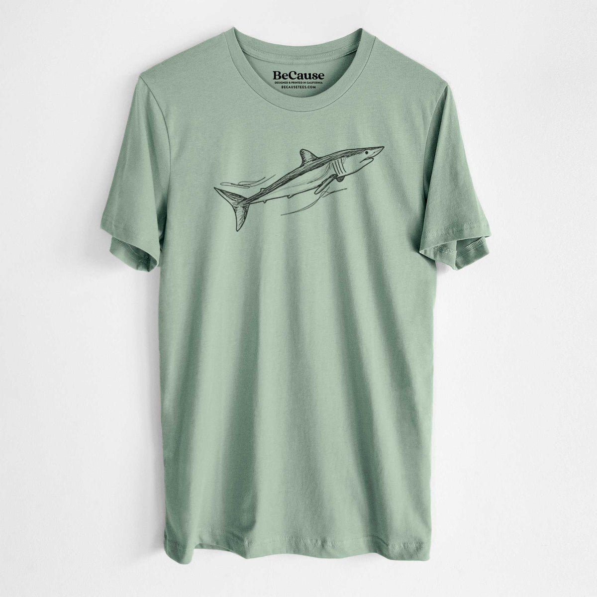 Sage green lightweight cotton t-shirt laid flat, printed with a black ink illustration of a mako shark swimming.