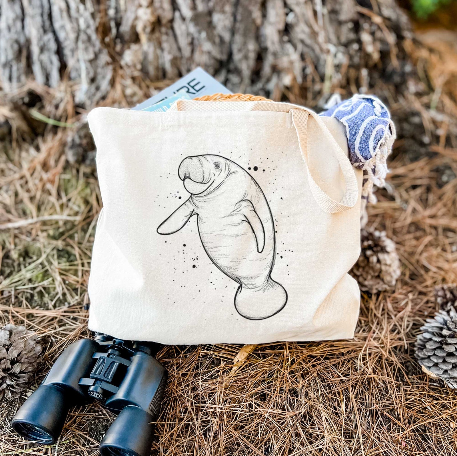Natural canvas tote bag printed with a black ink line drawing of a manatee swimming, with ink splatters.