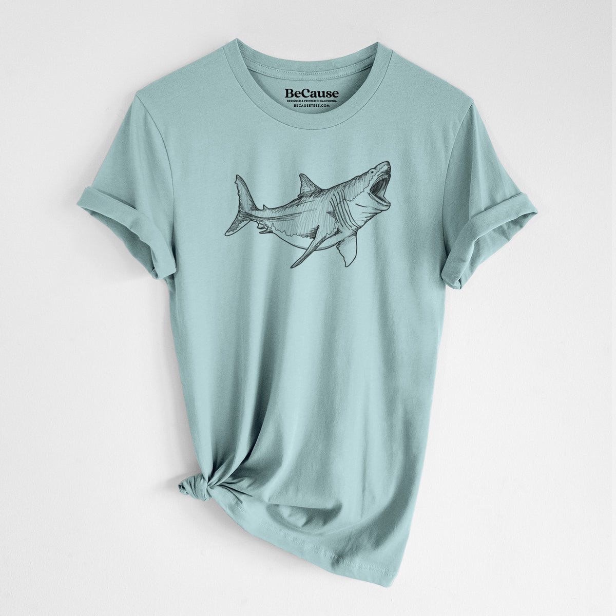 Dusty blue lightweight cotton t-shirt laid flat with the sleeves rolled, printed with a black ink illustration of a megalodon shark with its jaws open.
