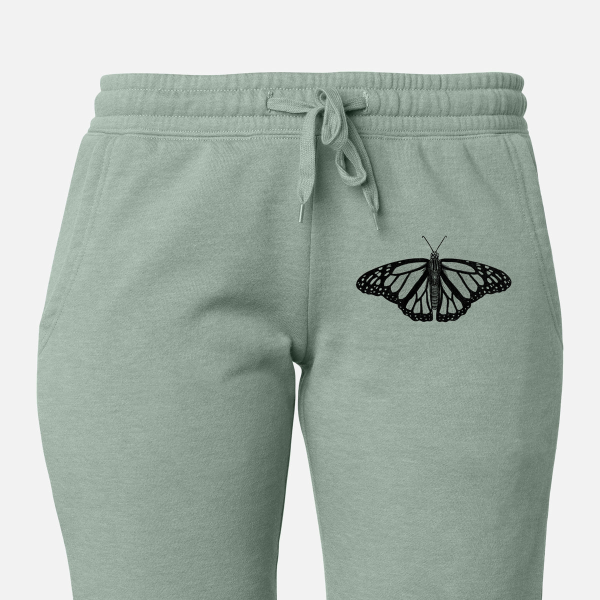 Front of sage green Cali Wave sweatpants, printed with a detailed black ink illustration of a monarch butterfly with its wings spread on the leg.