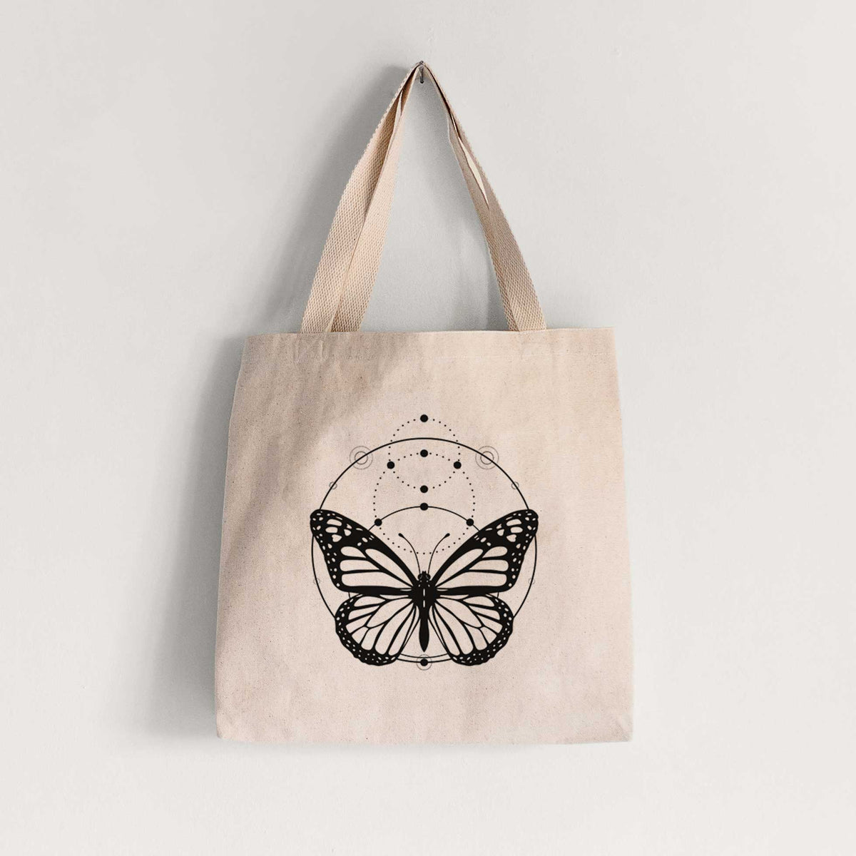 Natural canvas tote bag printed with a black ink monarch butterfly inside a circle, beneath a line of moon phases.