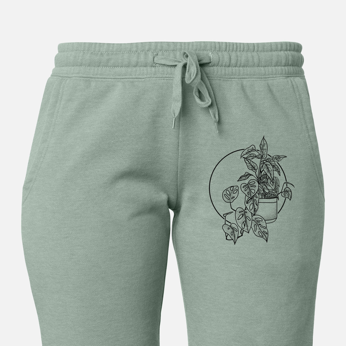 Front of sage green Cali Wave sweatpants, printed with a black ink illustration of a potted Monsteradansonii plant with trailing vines in front of a circle on the leg.