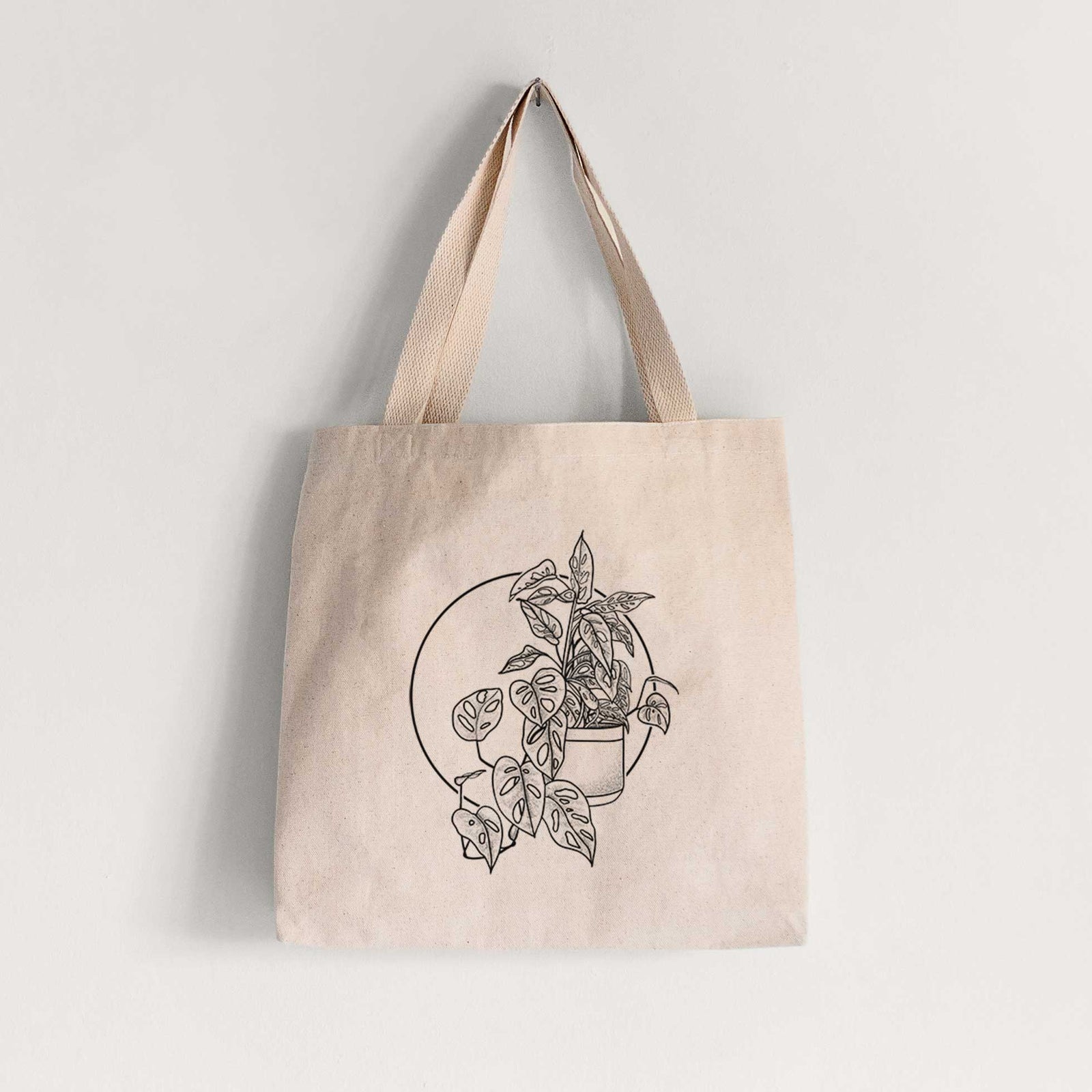 Natural canvas tote bag printed with a black ink illustration of a potted Monsteradansonii plant with trailing vines in front of a circle.