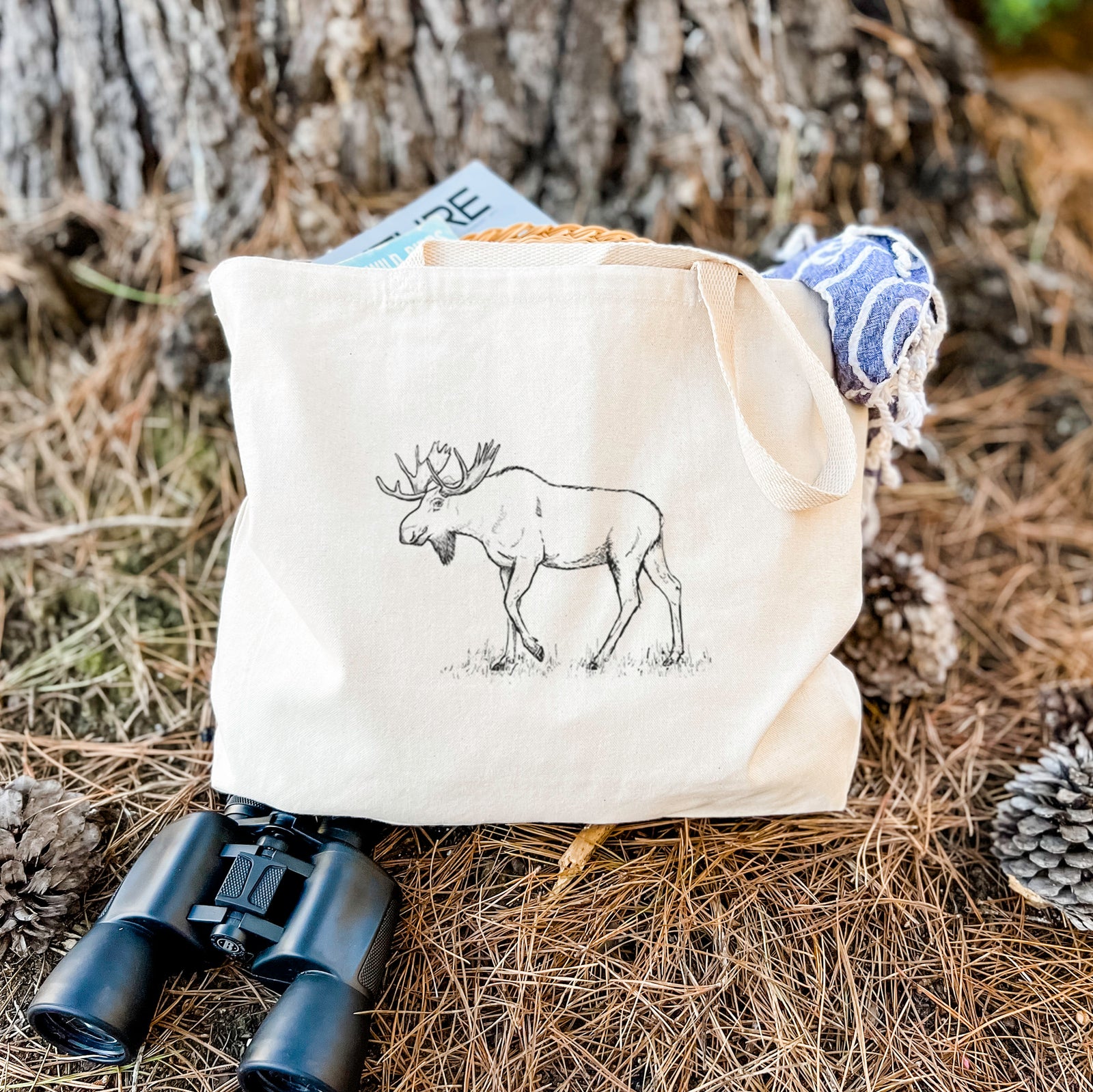 Natural canvas tote bag printed with a black ink illustration of a bull moose with broad antlers walking.
