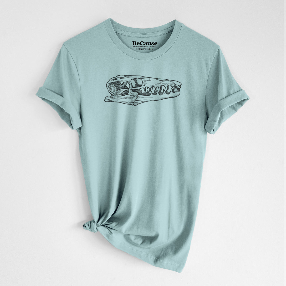 Dusty blue lightweight cotton t-shirt laid flat with the sleeves rolled, printed with a detailed black ink illustration of a Mosasaur skull.