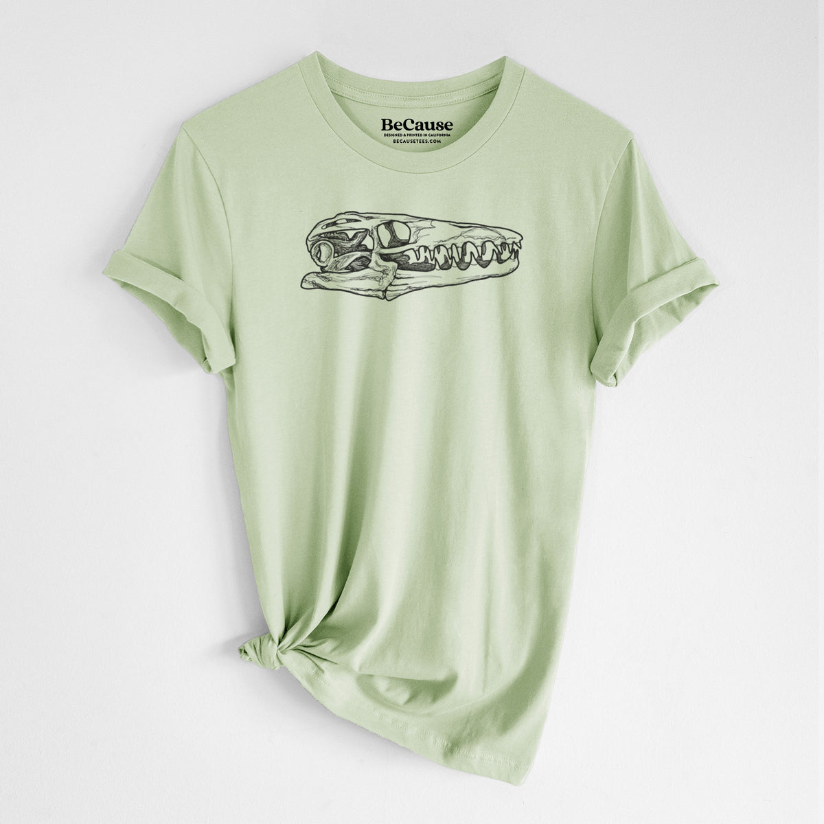Spring green lightweight cotton t-shirt laid flat with the sleeves rolled, printed with a detailed black ink illustration of a Mosasaur skull.