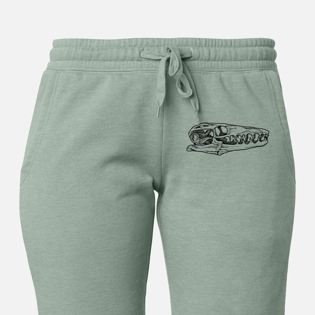 Front of sage green Cali Wave sweatpants, printed with a detailed black ink illustration of a Mosasaur skull on the leg.