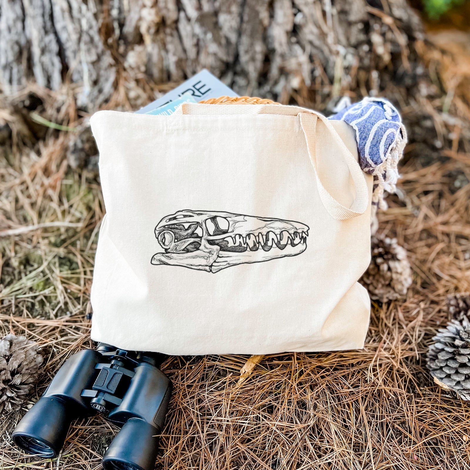 Natural canvas tote bag printed with a detailed black ink illustration of a Mosasaur skull.