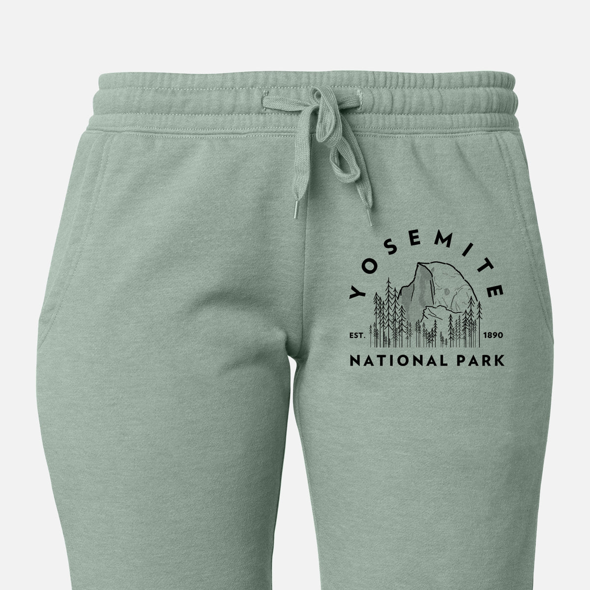 Front of sage green Cali Wave sweatpants, printed with a round badge of Half Dome and pine trees, with the words Yosemite National Park, Est. 1890 on the leg.