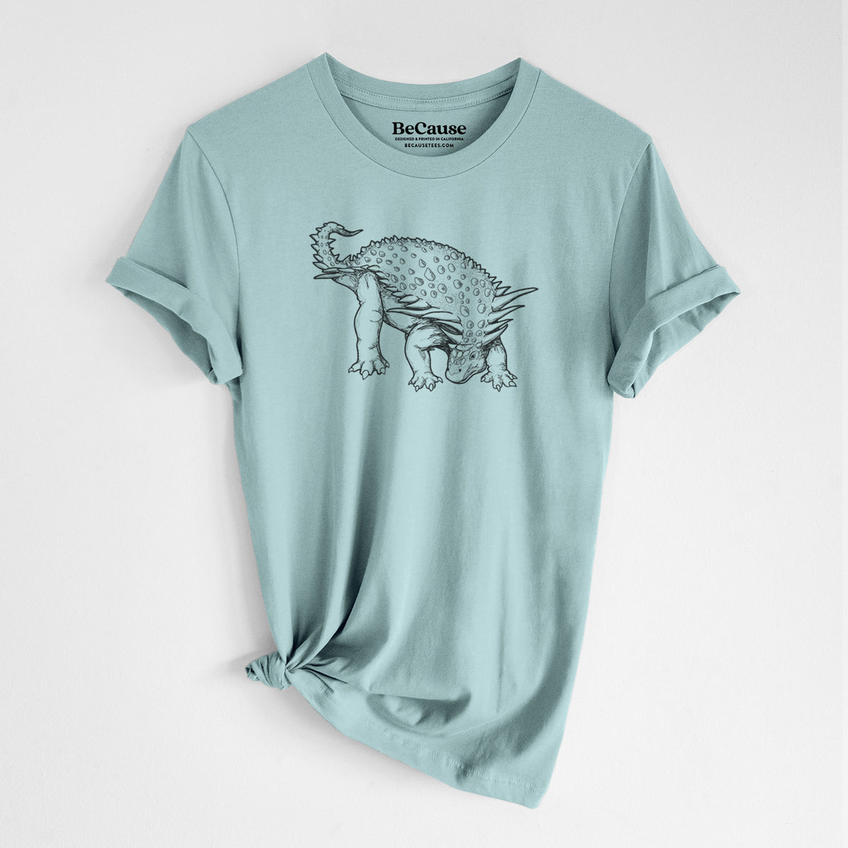 Dusty blue lightweight cotton t-shirt laid flat with the sleeves rolled, printed with a black ink illustration of an armored Nodosaurus.