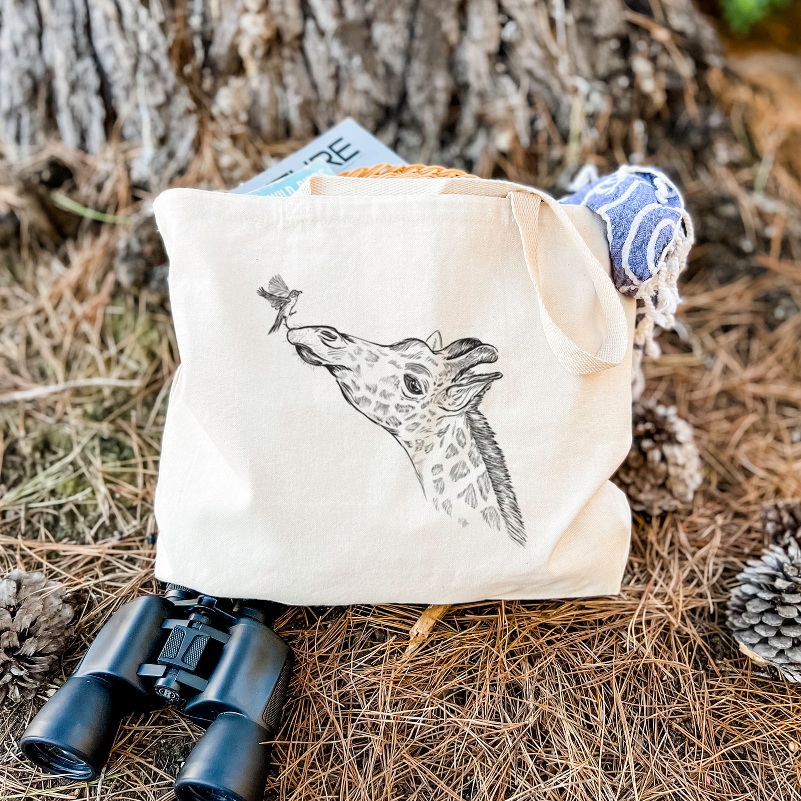 Natural canvas tote bag printed with a black ink illustration of a northern giraffe reaching its head up to nibble a flower.