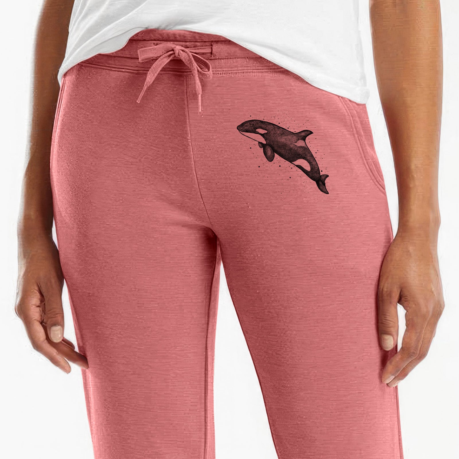 Front of dusty rose Cali Wave sweatpants, printed with a black ink illustration of an orca leaping, with ink splatters on the leg.