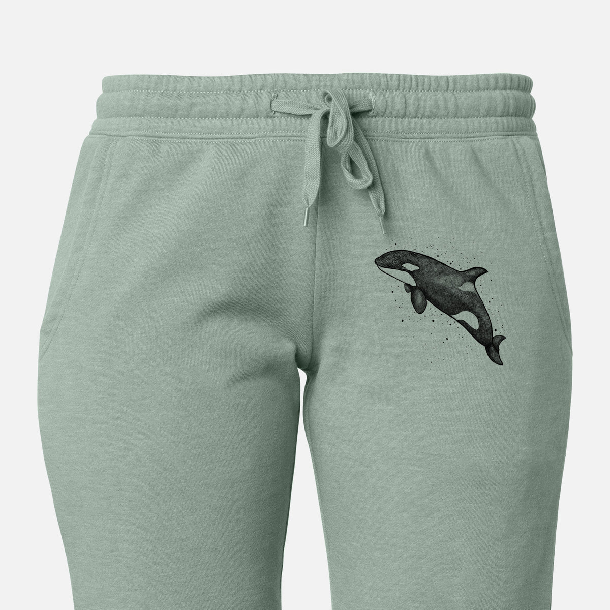 Front of sage green Cali Wave sweatpants, printed with a black ink illustration of an orca leaping, with ink splatters on the leg.