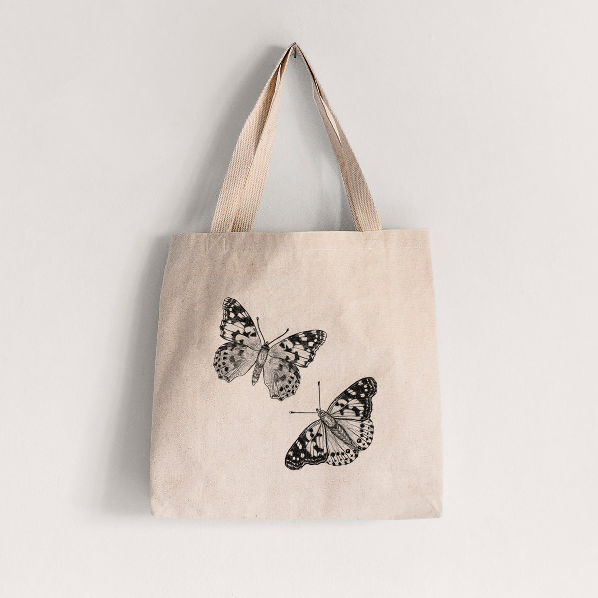 Natural canvas tote bag printed with a detailed black ink illustration of two painted lady butterflies.