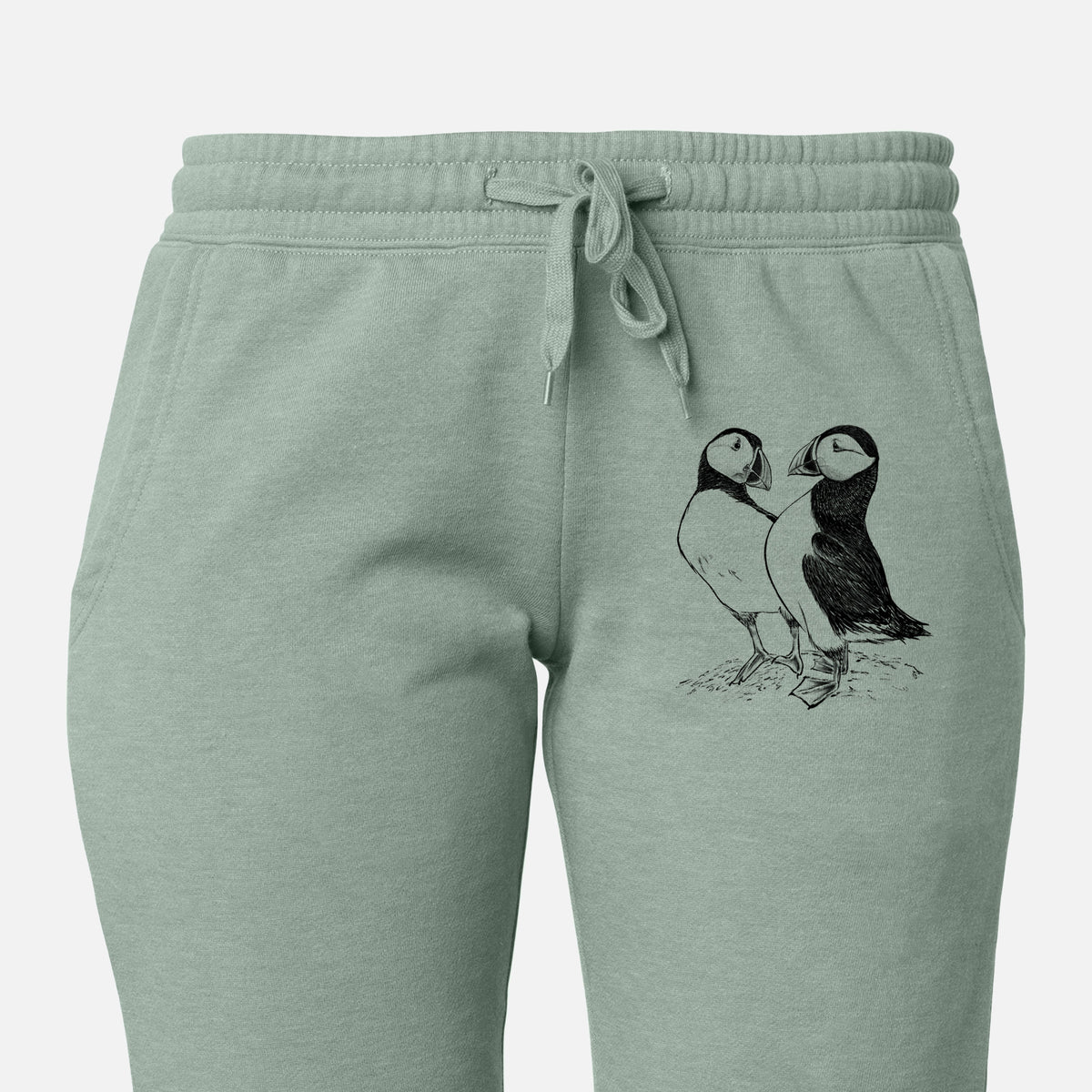 Front of sage green Cali Wave sweatpants, printed with a detailed black ink illustration of two Atlantic puffins standing side by side on the leg.