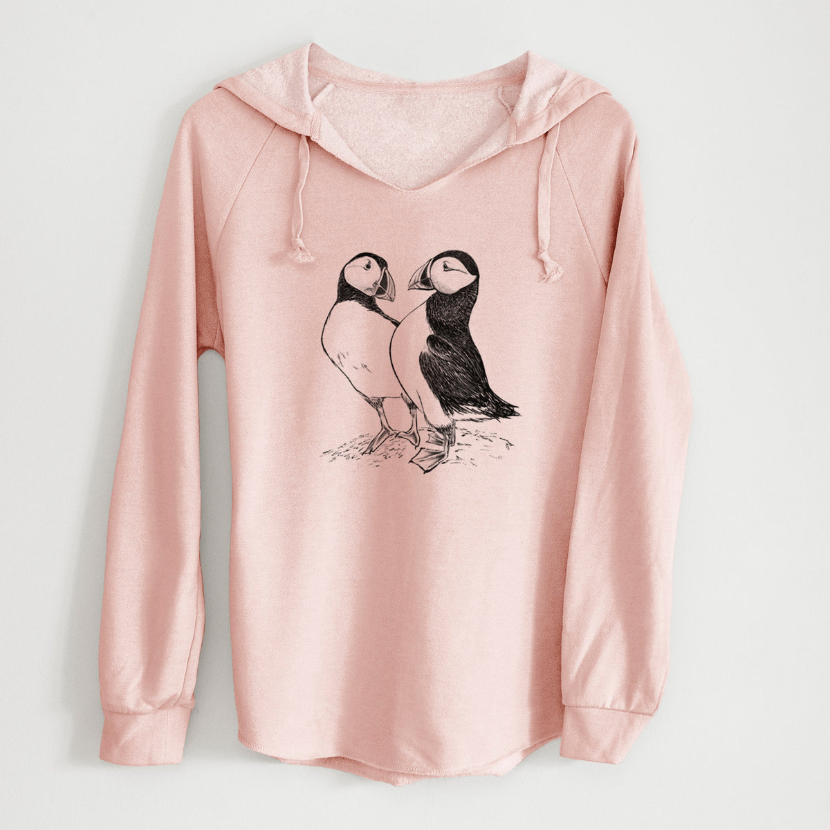 Blush pink women's Cali Wave hooded sweatshirt laid flat, printed with a detailed black ink illustration of two Atlantic puffins standing side by side.