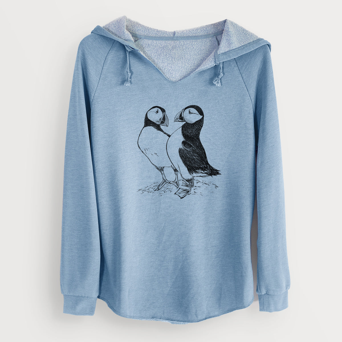 Misty blue women's Cali Wave hooded sweatshirt laid flat, printed with a detailed black ink illustration of two Atlantic puffins standing side by side.
