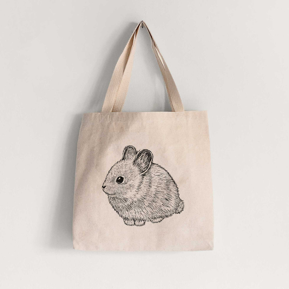 Natural canvas tote bag printed with a detailed black ink illustration of a round, fluffy pygmy rabbit.