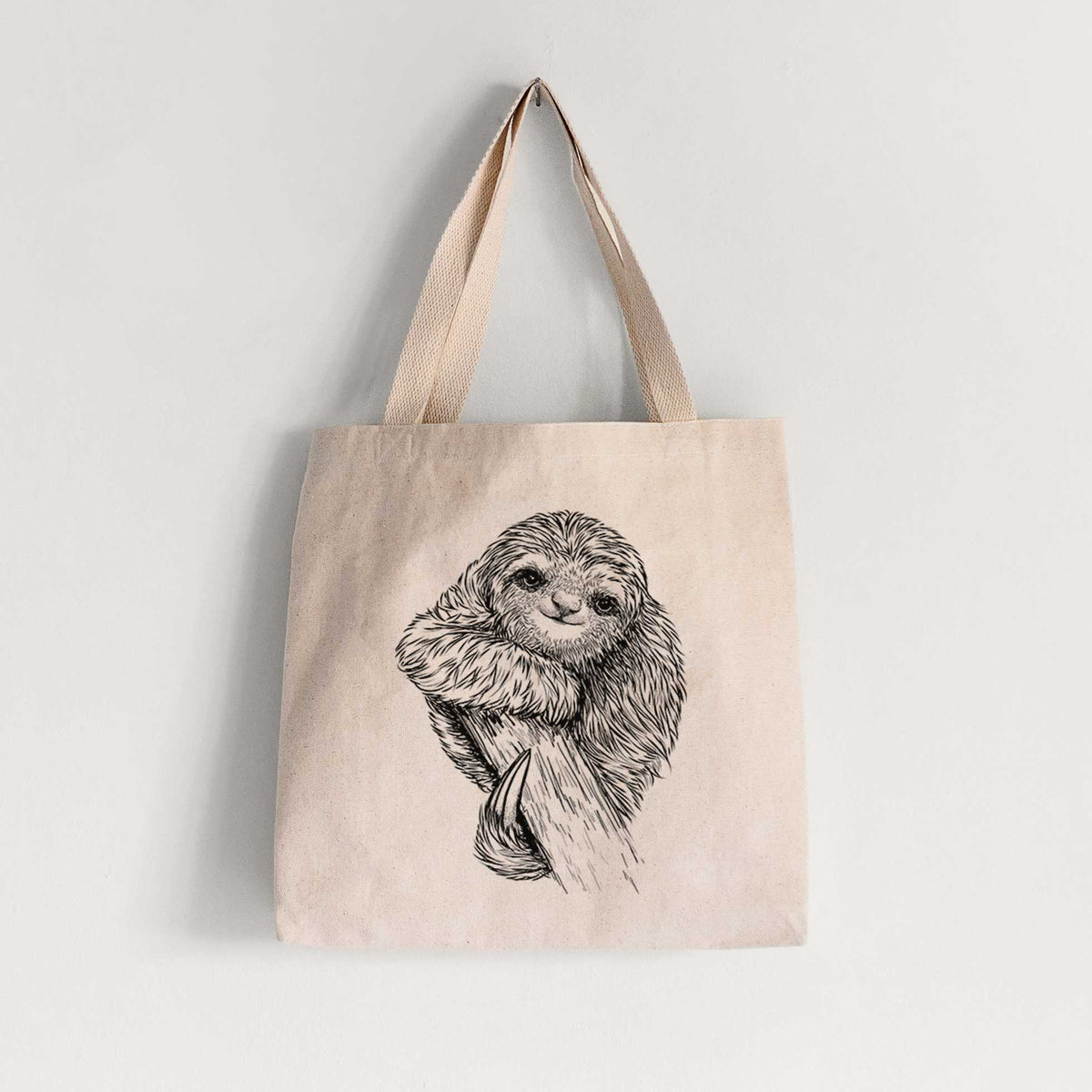 Natural canvas tote bag printed with a detailed black ink illustration of a smiling pygmy three-toed sloth hanging from a branch.