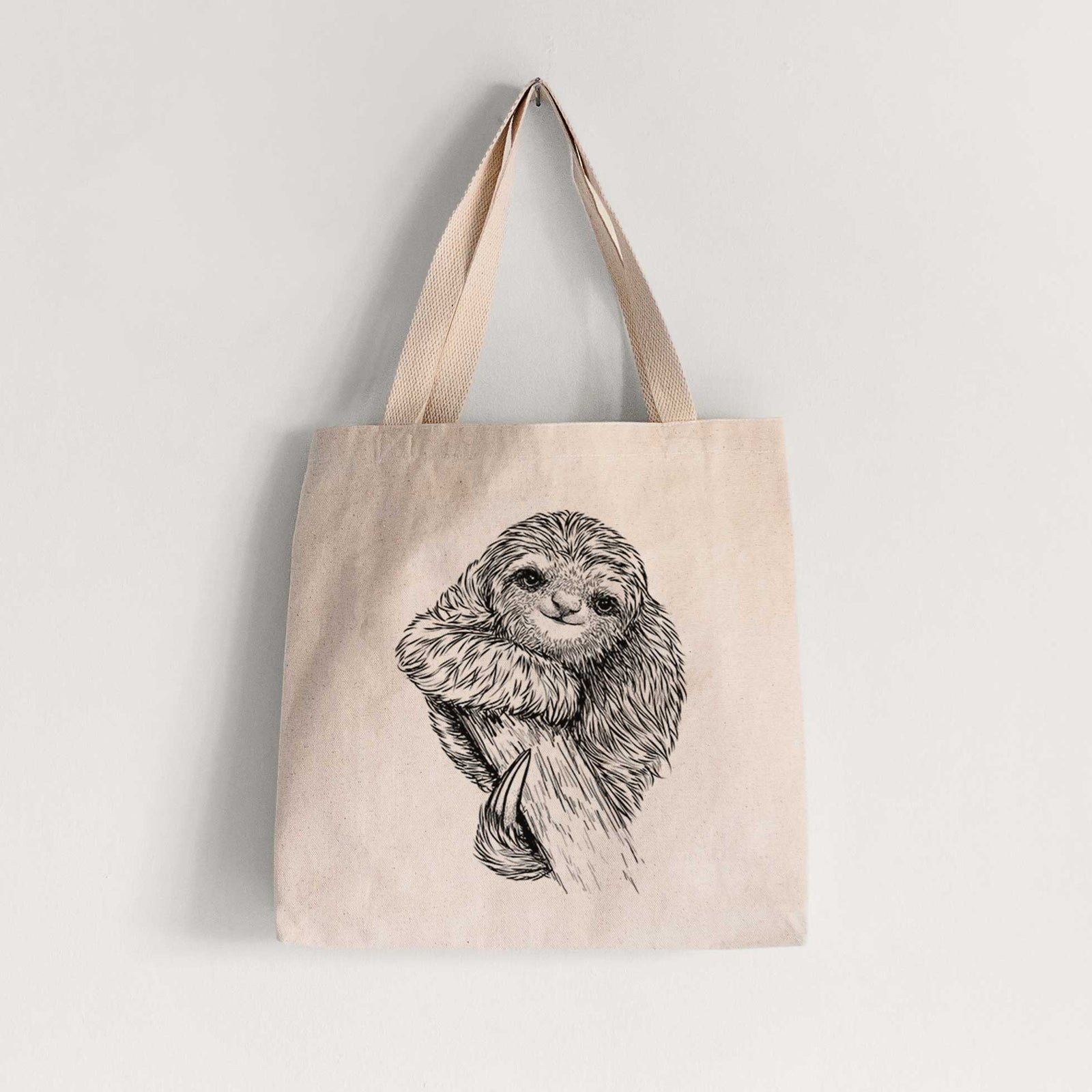 Natural canvas tote bag printed with a detailed black ink illustration of a smiling pygmy three-toed sloth hanging from a branch.