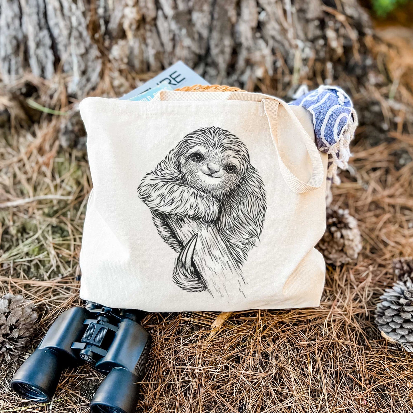 Natural canvas tote bag printed with a detailed black ink illustration of a smiling pygmy three-toed sloth hanging from a branch.