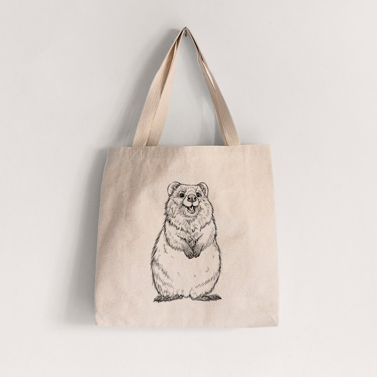 Natural canvas tote bag printed with a black ink illustration of a smiling quokka sitting upright.