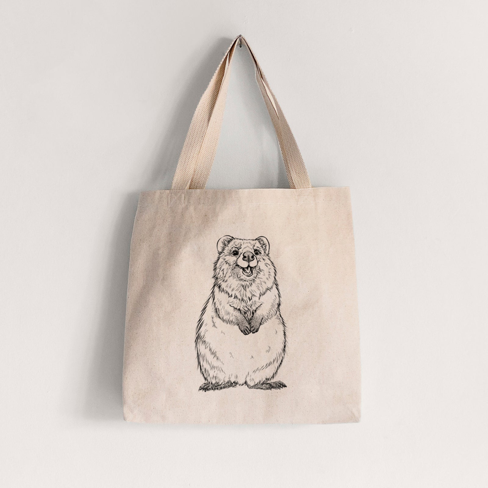 Natural canvas tote bag printed with a black ink illustration of a smiling quokka sitting upright.