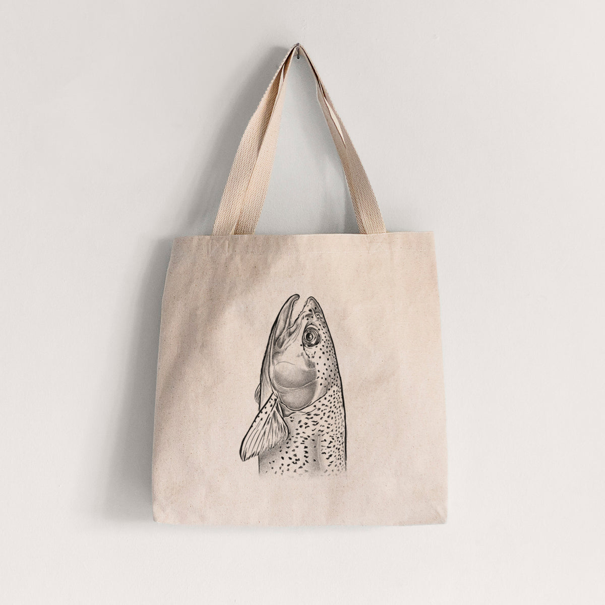Natural canvas tote bag printed with a detailed black ink illustration of a rainbow trout's head pointing upward, showing its spotted scales.