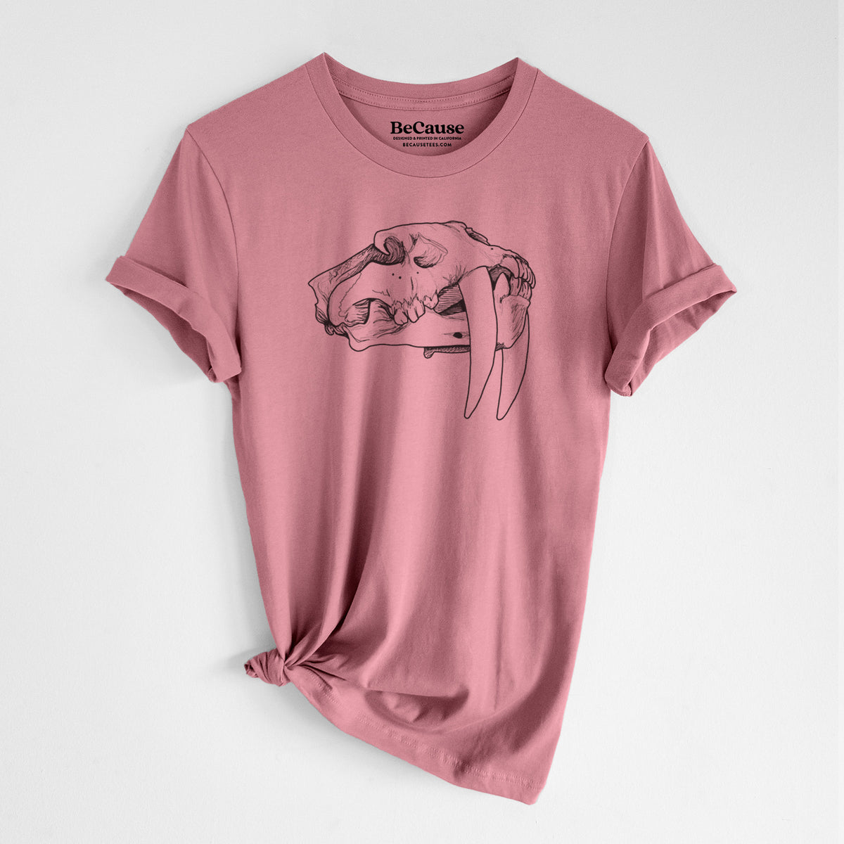 Mauve pink lightweight cotton t-shirt laid flat with the sleeves rolled, printed with a detailed black ink illustration of a saber-toothed tiger skull.