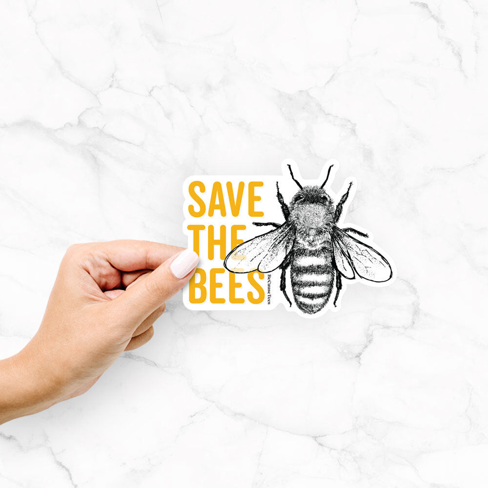 Hand holding a vinyl decal of yellow words reading Save the Bees beside a black ink honey bee.