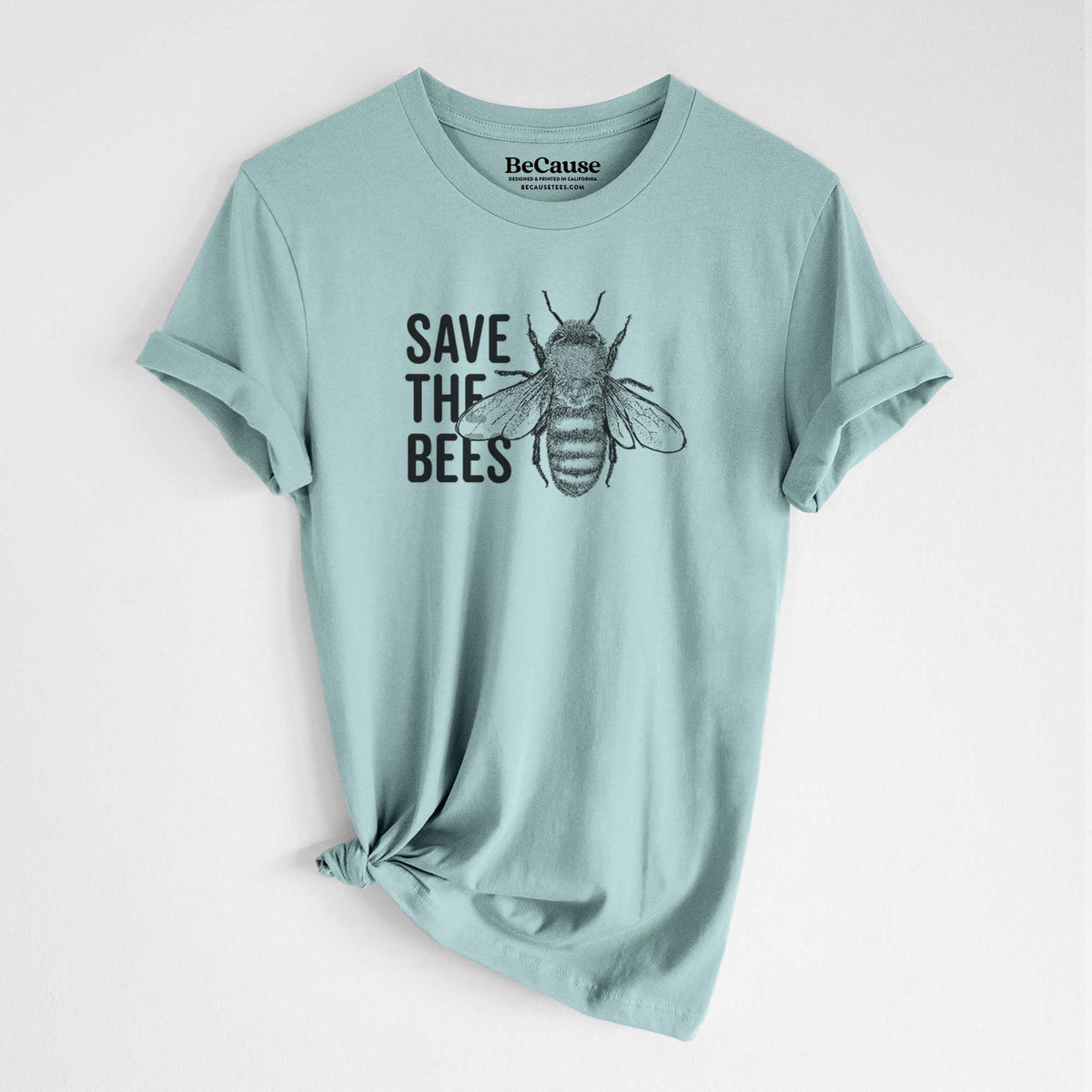 Dusty blue lightweight cotton t-shirt laid flat with the sleeves rolled, printed with bold black words reading Save the Bees beside a detailed honey bee illustration.