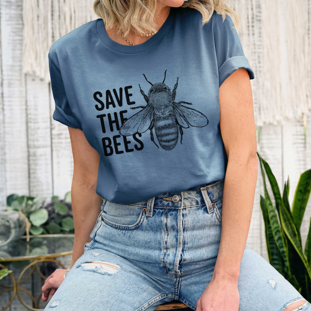 Woman wearing a steel blue lightweight cotton t-shirt printed with bold black words reading Save the Bees beside a detailed honey bee illustration.