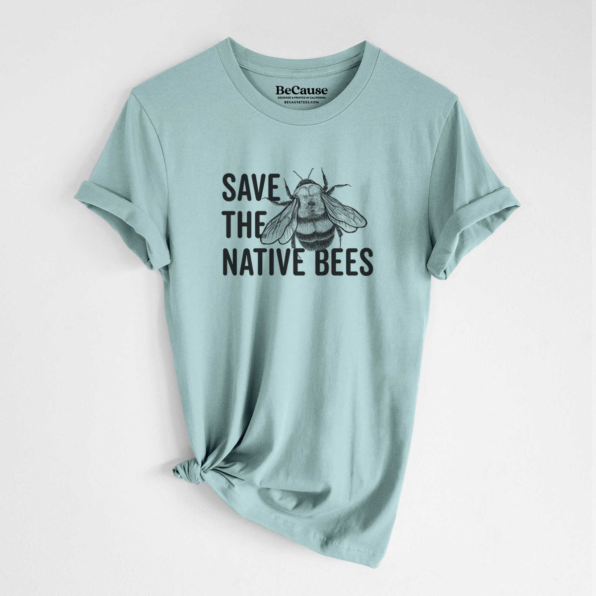 Dusty blue lightweight cotton t-shirt laid flat with the sleeves rolled, printed with bold black words reading Save the Native Bees beside a detailed bee illustration.