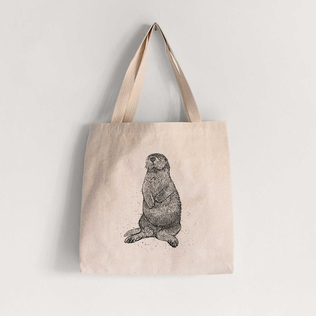 Natural canvas tote bag printed with a detailed black ink illustration of a sea otter sitting upright.