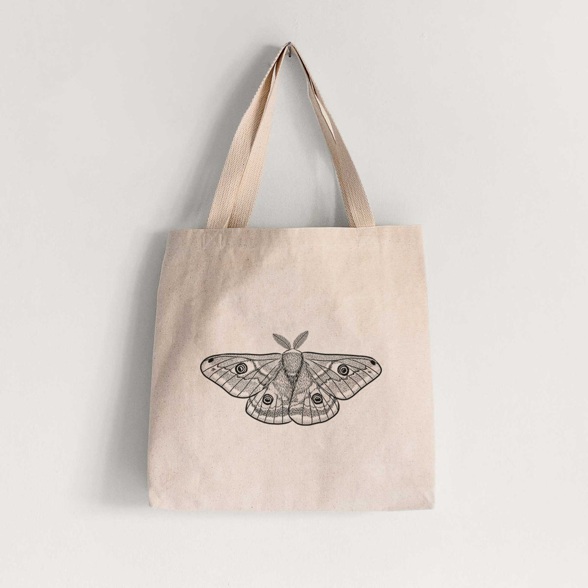Natural canvas tote bag printed with a detailed black ink illustration of a small emperor moth with eyespots on its wings.